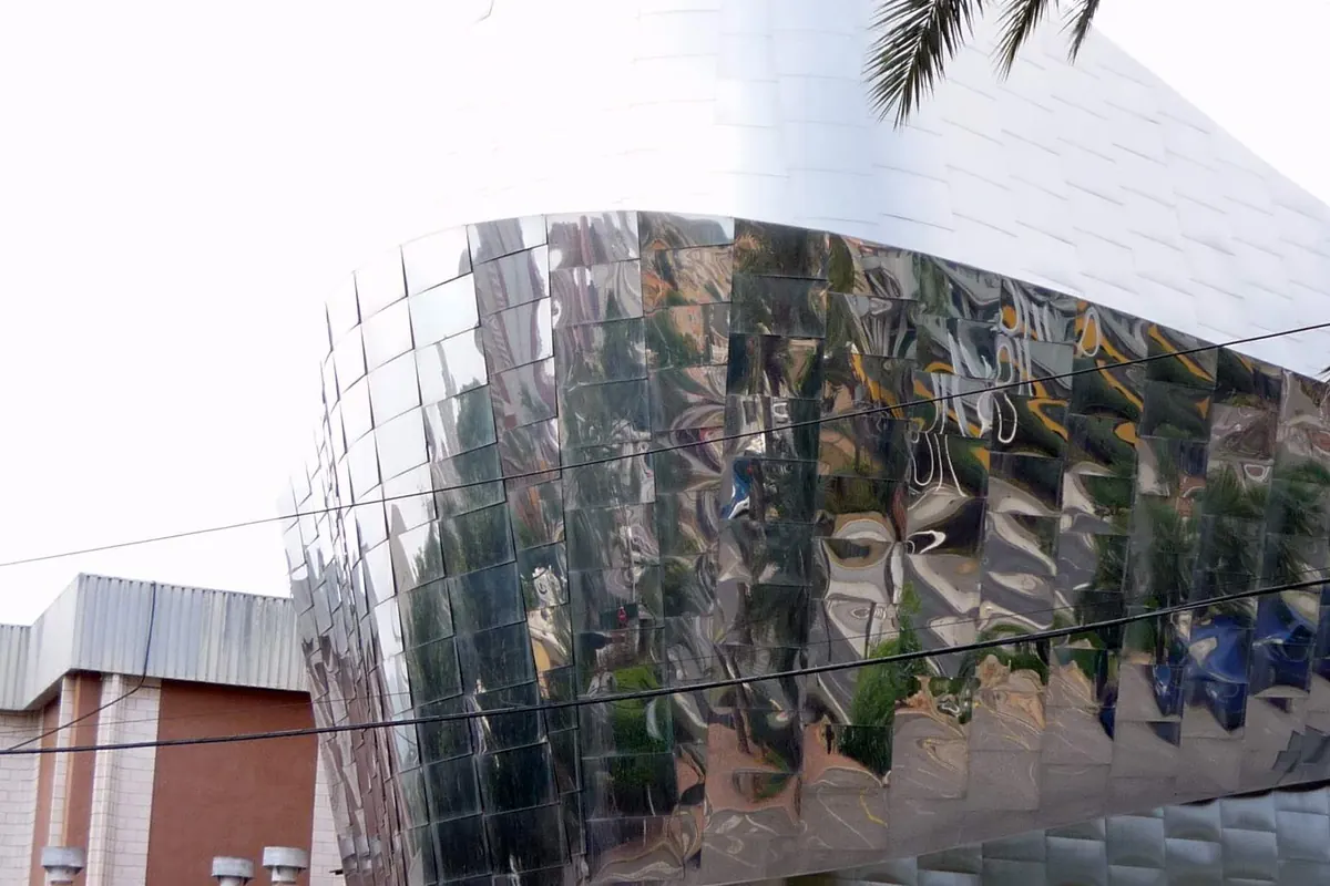Paneles pulidos de acero espejo en la esquina curva de Benidorm Palace, reflejando palmeras y la calle