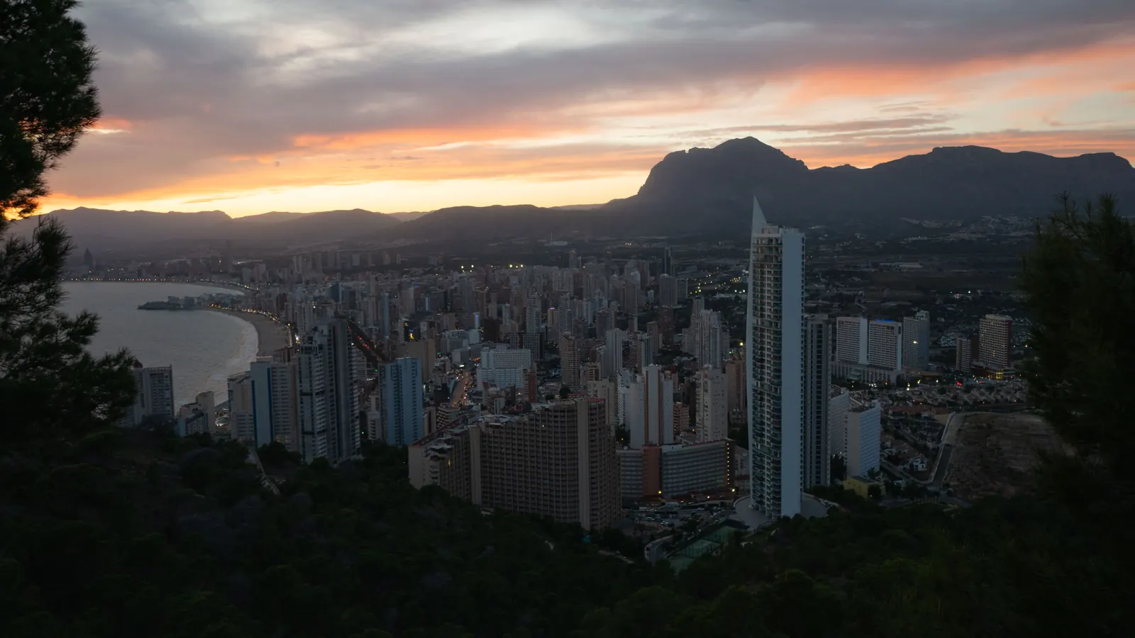 夕暮れの空の下に広がるベニドルムの高層ビル群と湾。街の背後には山の稜線